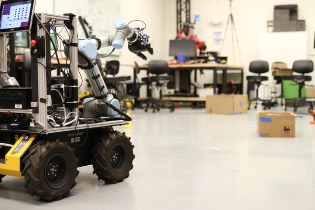 A mobile manipulator in a lab environment with boxes and other objects.